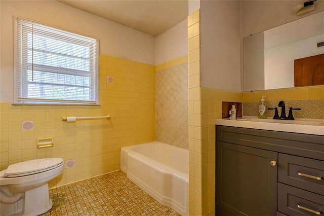 bathroom with a tub to relax in, toilet, vanity, tile patterned flooring, and tile walls