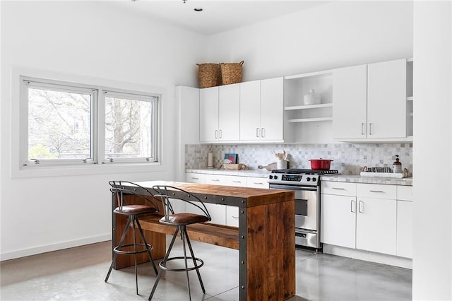 kitchen featuring concrete floors, baseboards, decorative backsplash, stainless steel gas stove, and open shelves