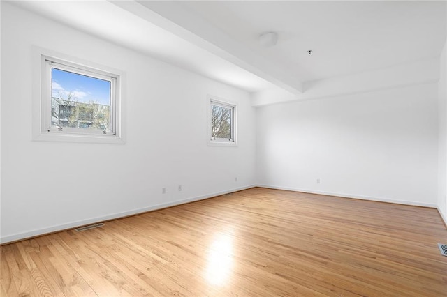 empty room with beam ceiling, baseboards, and light wood-type flooring