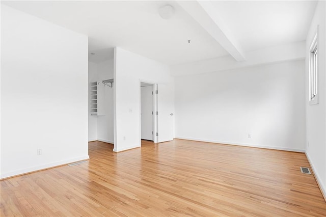 spare room featuring light wood finished floors, visible vents, baseboards, and beam ceiling