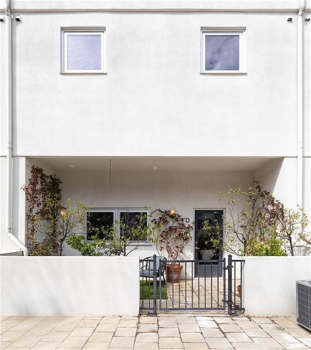 rear view of property featuring stucco siding, fence, and a gate