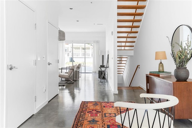 hall with stairs, finished concrete flooring, and baseboards