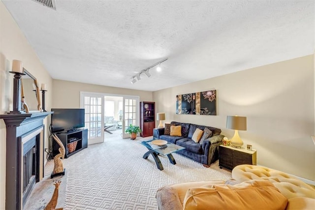 living room with carpet flooring, a textured ceiling, a fireplace with raised hearth, and rail lighting