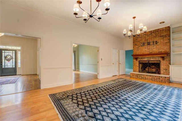 unfurnished living room with crown molding, a notable chandelier, wood-type flooring, a brick fireplace, and built in shelves