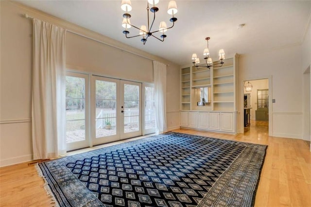 interior space with french doors, built in shelves, light hardwood / wood-style flooring, ornamental molding, and a notable chandelier