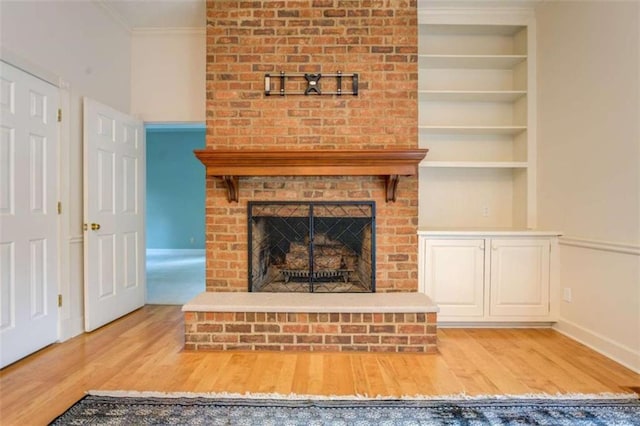 unfurnished living room featuring crown molding, a brick fireplace, light hardwood / wood-style floors, and built in shelves