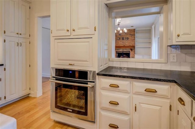 kitchen featuring a brick fireplace, oven, white cabinets, and light wood-type flooring