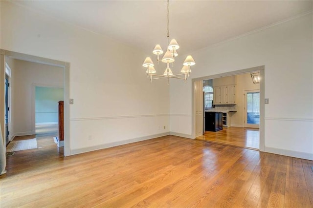 unfurnished living room with an inviting chandelier, crown molding, and light wood-type flooring