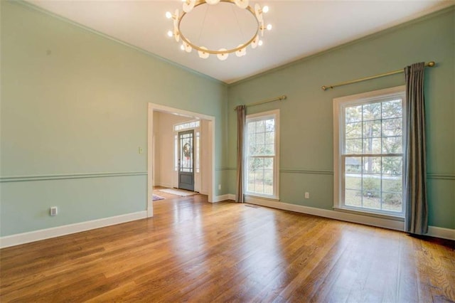 empty room with an inviting chandelier, plenty of natural light, ornamental molding, and light wood-type flooring