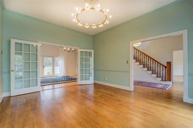 spare room featuring an inviting chandelier, hardwood / wood-style flooring, ornamental molding, and french doors