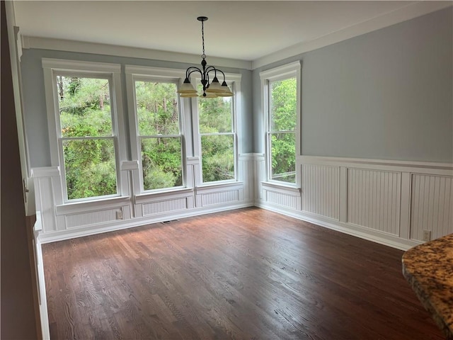unfurnished dining area with a chandelier, a decorative wall, wainscoting, and dark wood-style floors