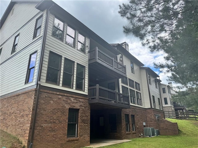 view of side of property featuring a balcony, central AC unit, brick siding, and a yard