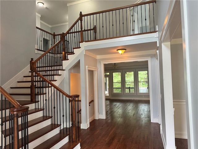 stairs featuring wood finished floors, baseboards, crown molding, and a high ceiling