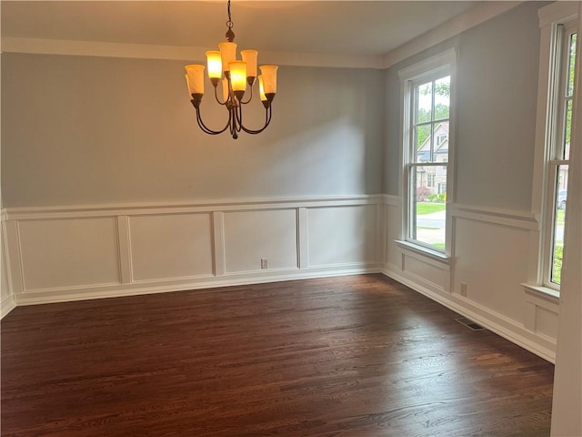 unfurnished dining area featuring a chandelier, a decorative wall, dark wood finished floors, and a wainscoted wall