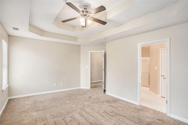 carpeted empty room featuring a textured ceiling, a raised ceiling, and ceiling fan