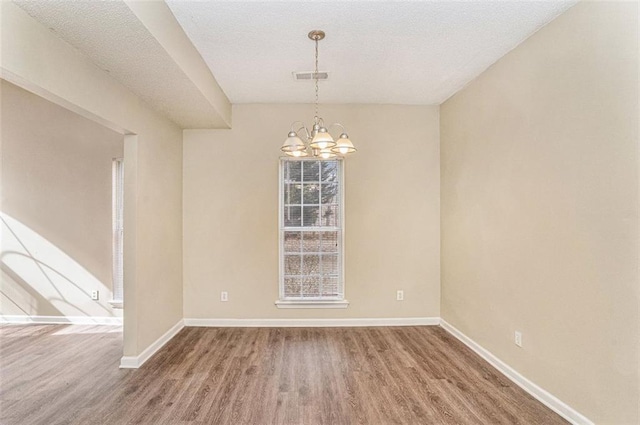 spare room with an inviting chandelier and wood-type flooring