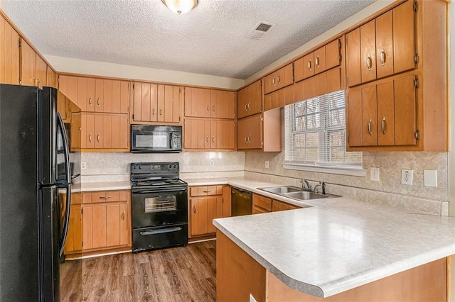 kitchen featuring sink, wood-type flooring, black appliances, kitchen peninsula, and backsplash