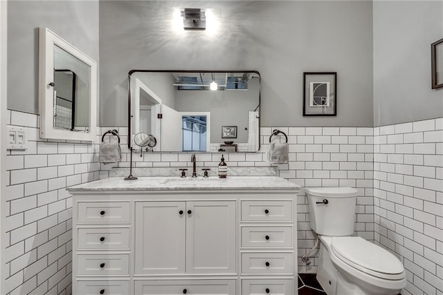 bathroom featuring wainscoting, tile walls, toilet, and vanity