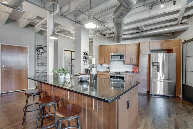 kitchen featuring a kitchen bar, appliances with stainless steel finishes, dark wood finished floors, and backsplash