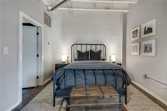 bedroom with baseboards, brick wall, visible vents, and wood finished floors