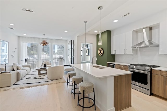 kitchen featuring white cabinetry, sink, wall chimney range hood, a kitchen island with sink, and high end range