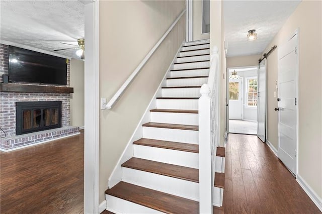 stairs with ceiling fan, a fireplace, wood-type flooring, a textured ceiling, and a barn door