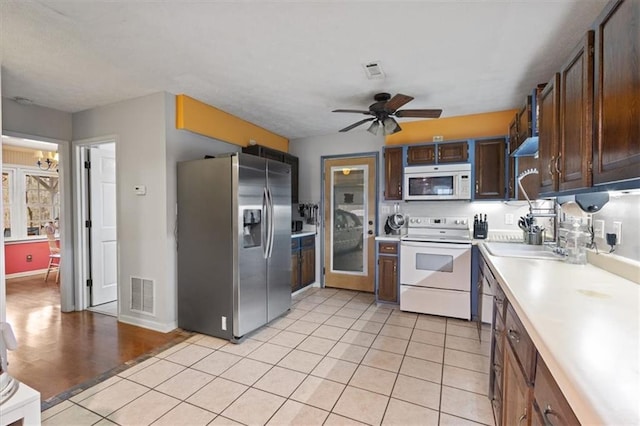 kitchen with white appliances, sink, ceiling fan, light tile patterned flooring, and dark brown cabinetry