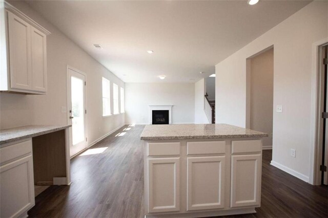 kitchen with light stone countertops, dark wood-type flooring, white cabinetry, and a kitchen island