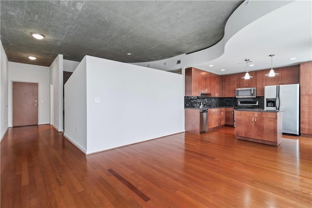 kitchen featuring a center island, tasteful backsplash, hardwood / wood-style floors, decorative light fixtures, and appliances with stainless steel finishes