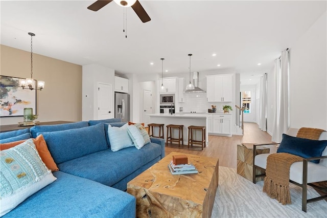 living room with ceiling fan with notable chandelier and light hardwood / wood-style flooring