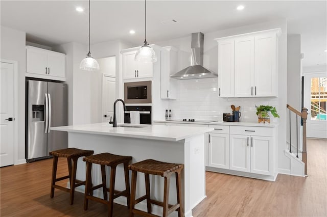 kitchen featuring black appliances, white cabinets, wall chimney range hood, and sink