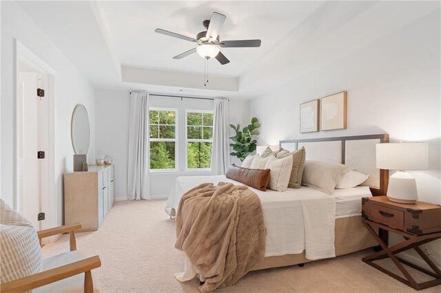 carpeted bedroom with a raised ceiling and ceiling fan