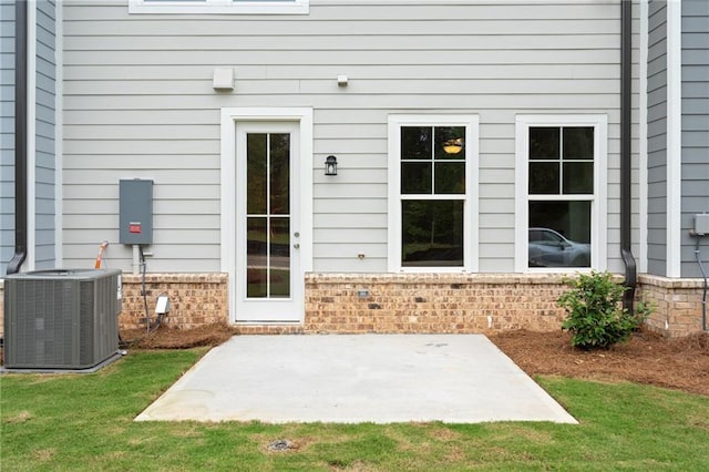 entrance to property featuring a lawn, a patio area, and cooling unit