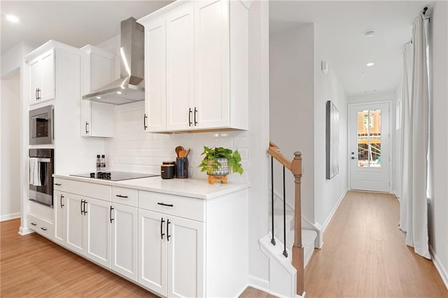 kitchen featuring white cabinetry, wall chimney exhaust hood, backsplash, appliances with stainless steel finishes, and light wood-type flooring