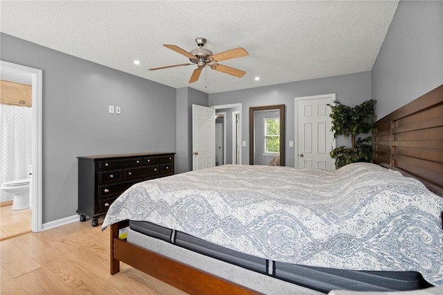 bedroom with baseboards, light wood-style floors, ensuite bath, and a textured ceiling