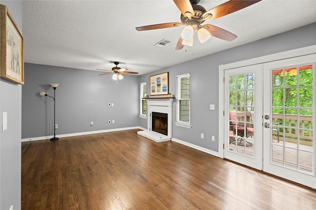 unfurnished living room featuring wood finished floors, french doors, a ceiling fan, visible vents, and a fireplace with raised hearth
