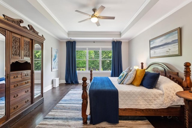 bedroom with a raised ceiling, dark wood-style floors, crown molding, a ceiling fan, and baseboards