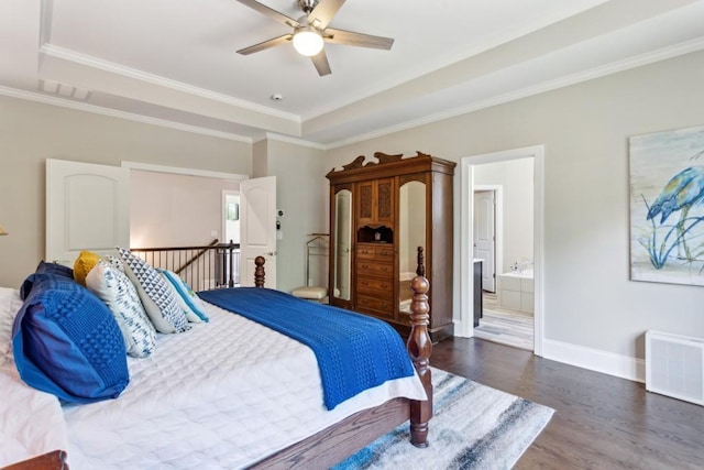 bedroom featuring wood finished floors, crown molding, a raised ceiling, baseboards, and ensuite bathroom