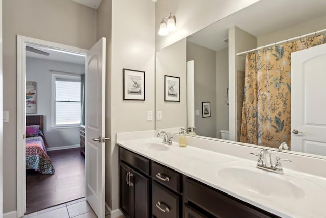 ensuite bathroom with toilet, double vanity, tile patterned flooring, and baseboards