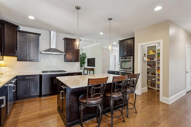 kitchen with wall chimney exhaust hood, stainless steel appliances, wood finished floors, a center island, and recessed lighting