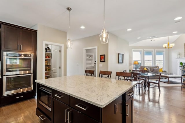 kitchen with stainless steel appliances, wood finished floors, pendant lighting, a kitchen island, and dark brown cabinets