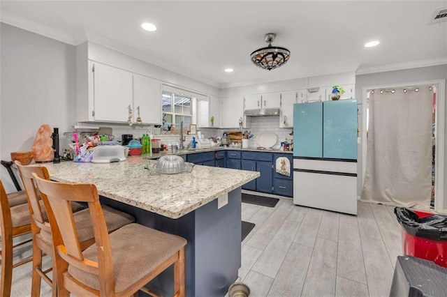 kitchen with kitchen peninsula, decorative backsplash, a kitchen breakfast bar, blue cabinets, and white cabinets