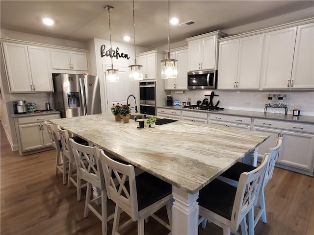 kitchen with a kitchen bar, white cabinetry, a large island with sink, pendant lighting, and stainless steel appliances