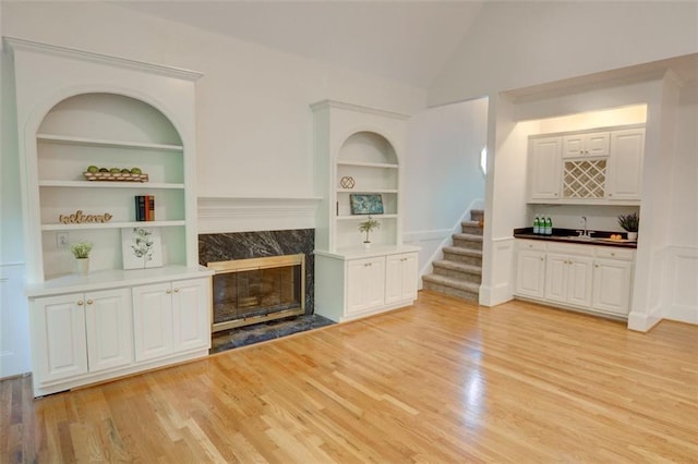 5404 Chaversham Ln, Peachtree Corners, GA 30092 - unfurnished living room with built in shelves, bar with sink, light wood finished floors, a premium fireplace, and high vaulted ceiling