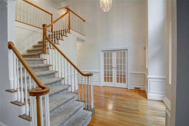 5404 Chaversham Ln, Peachtree Corners, GA 30092 - staircase featuring wood finished floors, french doors, a decorative wall, a towering ceiling, and wainscoting
