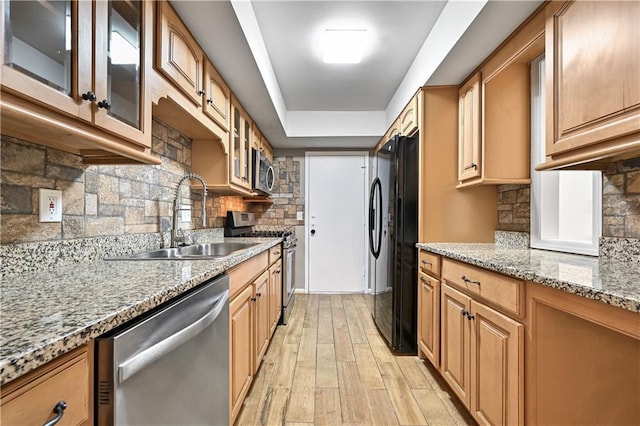 kitchen with sink, light stone counters, stainless steel appliances, light hardwood / wood-style floors, and decorative backsplash