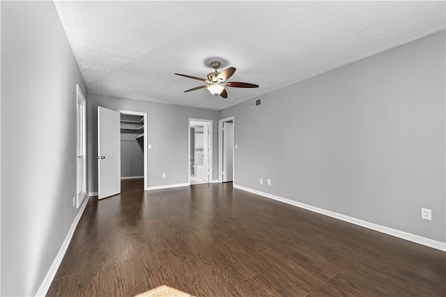 unfurnished bedroom featuring dark wood-type flooring, ceiling fan, a textured ceiling, a walk in closet, and a closet