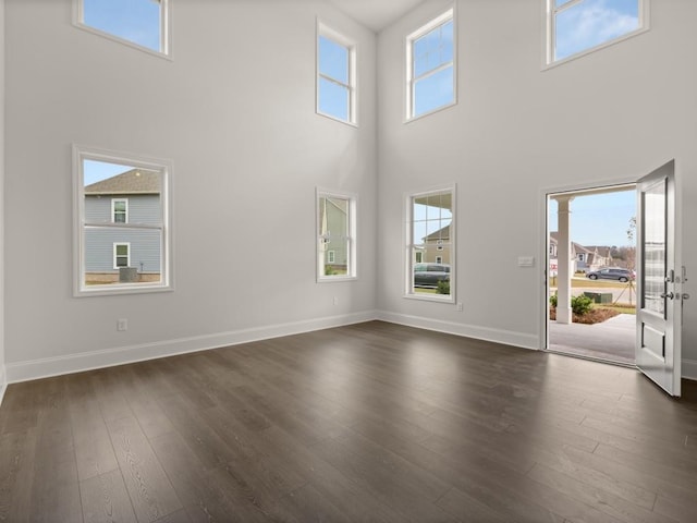 unfurnished living room with a high ceiling, baseboards, and dark wood-type flooring