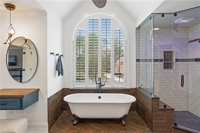 full bath with lofted ceiling, a wainscoted wall, a soaking tub, and a stall shower