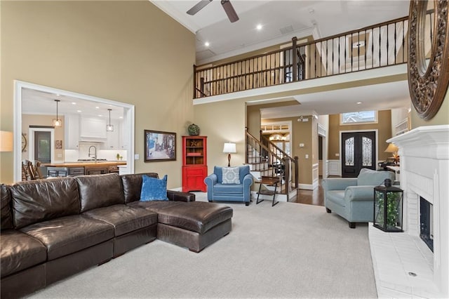 living room with light colored carpet, a fireplace, a towering ceiling, stairs, and ornamental molding